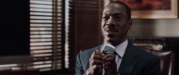 Movie still from “Imagine That” (2009), directed by Karey Kirkpatrick – A man in a suit and tie holding a microphone in his hand; Close Up shot, Low angle