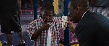 Movie still from “Imagine That” (2009), directed by Karey Kirkpatrick – A man holding a dollar bill in front of a young man; Medium shot, Over the shoulder angle