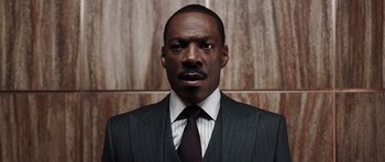 Movie still from “Imagine That” (2009), directed by Karey Kirkpatrick – A man wearing a suit and tie in front of a wooden wall; Close Up shot, Low angle