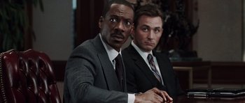 Movie still from “Imagine That” (2009), directed by Karey Kirkpatrick – A man in a suit sitting next to another man in a suit; Close Up shot, Over the shoulder angle