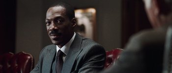 Movie still from “Imagine That” (2009), directed by Karey Kirkpatrick – A man in a suit and tie sitting in a chair; Close Up shot, Over the shoulder angle