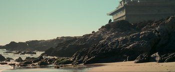 Movie still from “Inception” (2010), directed by Christopher Nolan – A person sitting on a rock on the beach; Extreme Wide shot, Low angle