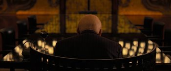 Movie still from “Inception” (2010), directed by Christopher Nolan – An older man sitting on a bench in front of a screen; Medium shot, Over the shoulder angle