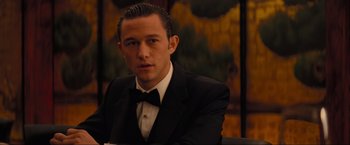 Movie still from “Inception” (2010), directed by Christopher Nolan – A man in a tuxedo sitting in front of a painting; Close Up shot, Over the shoulder angle