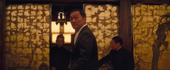 Movie still from “Inception” (2010), directed by Christopher Nolan – A man in a black suit standing next to two other men; Medium shot, Low angle