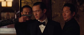 Movie still from “Inception” (2010), directed by Christopher Nolan – A man in a tuxedo holding a gun in front of another man in a suit; Close Up shot, Over the shoulder angle