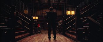 Movie still from “Inception” (2010), directed by Christopher Nolan – A man in a suit standing in front of stairs; Wide shot, Low angle