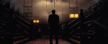 Movie still from “Inception” (2010), directed by Christopher Nolan – A man in a suit standing in front of some lights; Wide shot, Low angle