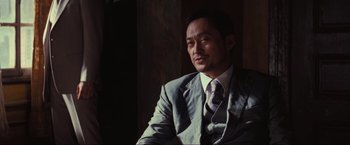 Movie still from “Inception” (2010), directed by Christopher Nolan – A man wearing a suit and tie sitting in a room; Close Up shot, Low angle