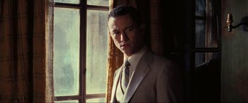 Movie still from “Inception” (2010), directed by Christopher Nolan – A man wearing a suit and tie standing in front of a window; Close Up shot, Over the shoulder angle