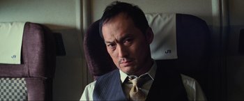 Movie still from “Inception” (2010), directed by Christopher Nolan – A person sitting on a chair wearing a tie; Close Up shot, Low angle