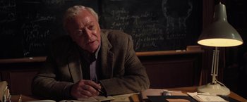 Movie still from “Inception” (2010), directed by Christopher Nolan – An older man sitting in front of a chalkboard; Medium shot, Over the shoulder angle