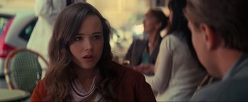 Movie still from “Inception” (2010), directed by Christopher Nolan – A woman sitting on a chair in a room with other people; Close Up shot, Over the shoulder angle