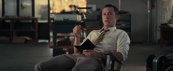 Movie still from “Inception” (2010), directed by Christopher Nolan – A man sitting in a chair holding a pen and a notebook; Medium shot, High angle