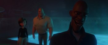 Movie still from “Incredibles 2” (2018), directed by Brad Bird – Two men standing in a dark room with a light shining on them; Medium shot, Over the shoulder angle