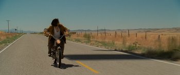 Movie still from “Independence Day” (1996), directed by Roland Emmerich – A person riding a motorcycle down the middle of a road; Wide shot, Low angle