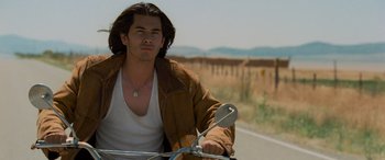 Movie still from “Independence Day” (1996), directed by Roland Emmerich – A man riding on the back of a motorcycle down a road; Medium shot, Low angle