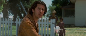 Movie still from “Independence Day” (1996), directed by Roland Emmerich – A man with long brown hair and a cowboy hat; Close Up shot, Over the shoulder angle