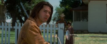 Movie still from “Independence Day” (1996), directed by Roland Emmerich – A man with long brown hair standing in front of a white fence; Close Up shot, Over the shoulder angle