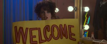 Movie still from “Independence Day” (1996), directed by Roland Emmerich – A woman holding a sign that says " welcome "; Medium shot, Over the shoulder angle