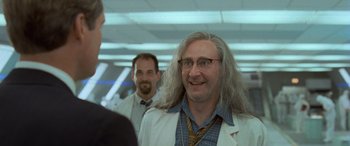 Movie still from “Independence Day” (1996), directed by Roland Emmerich – A man with long white hair is smiling for the camera; Medium shot, Over the shoulder angle