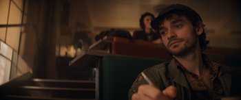 Movie still from “Indiana Jones and the Dial of Destiny” (2023), directed by James Mangold – A man sitting at a table in front of a group of people; Close Up shot, Over the shoulder angle