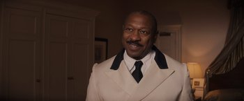 Movie still from “Indiana Jones and the Dial of Destiny” (2023), directed by James Mangold – A man in a white suit and black tie smiling; Medium shot, Over the shoulder angle