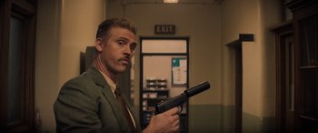 Movie still from “Indiana Jones and the Dial of Destiny” (2023), directed by James Mangold – A man in a suit and tie holding a gun in a room; Close Up shot, Low angle