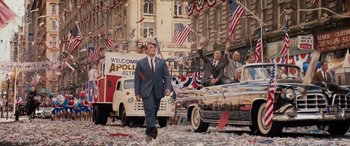 Movie still from “Indiana Jones and the Dial of Destiny” (2023), directed by James Mangold – A man in a suit and tie walking in a parade; Wide shot, High angle