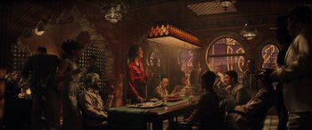 Movie still from “Indiana Jones and the Dial of Destiny” (2023), directed by James Mangold – A group of people sitting around a table with food on top of it; Wide shot, Over the shoulder angle