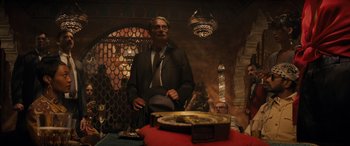 Movie still from “Indiana Jones and the Dial of Destiny” (2023), directed by James Mangold – A man in a suit and tie standing in front of a table; Medium shot, Over the shoulder angle