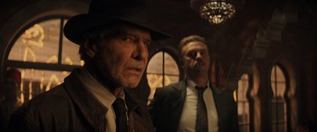 Movie still from “Indiana Jones and the Dial of Destiny” (2023), directed by James Mangold – Two men in suits and hats standing next to each other in a room; Medium shot, Over the shoulder angle