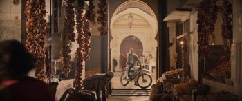 Movie still from “Indiana Jones and the Dial of Destiny” (2023), directed by James Mangold – A man riding a bike through a doorway; Wide shot, Over the shoulder angle
