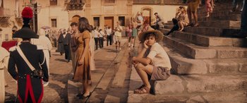 Movie still from “Indiana Jones and the Dial of Destiny” (2023), directed by James Mangold – A young boy wearing a straw hat sitting on steps; Wide shot, High angle