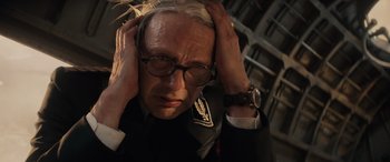 Movie still from “Indiana Jones and the Dial of Destiny” (2023), directed by James Mangold – An older man in a suit and glasses holding his head with both hands; Close Up shot, High angle