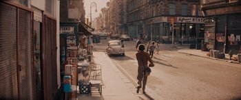 Movie still from “Indiana Jones and the Dial of Destiny” (2023), directed by James Mangold – A woman walking down a street past a store; Wide shot, High angle