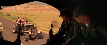 Movie still from “Indiana Jones and the Kingdom of the Crystal Skull” (2008), directed by Steven Spielberg – Two men sitting in the back of a car on the side of the road; Wide shot, Over the shoulder angle