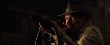 Movie still from “Indiana Jones and the Kingdom of the Crystal Skull” (2008), directed by Steven Spielberg – A man in a hat holding a gun in a dark room; Close Up shot, Low angle