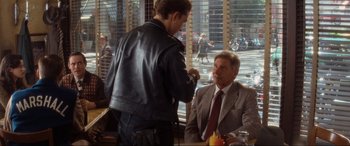 Movie still from “Indiana Jones and the Kingdom of the Crystal Skull” (2008), directed by Steven Spielberg – A man in a suit and tie sitting at a table with another man; Medium shot, Over the shoulder angle