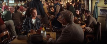 Movie still from “Indiana Jones and the Kingdom of the Crystal Skull” (2008), directed by Steven Spielberg – A group of people sitting at a table with drinks; Medium shot, Over the shoulder angle