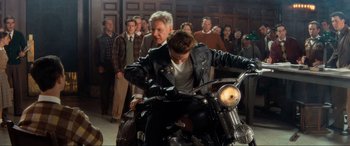 Movie still from “Indiana Jones and the Kingdom of the Crystal Skull” (2008), directed by Steven Spielberg – A man riding a motorcycle in front of a group of people; Wide shot, Over the shoulder angle