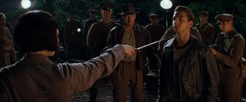 Movie still from “Indiana Jones and the Kingdom of the Crystal Skull” (2008), directed by Steven Spielberg – A group of people in a field with a person holding a sword; Medium shot, Over the shoulder angle