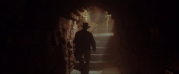 Movie still from “Indiana Jones and the Kingdom of the Crystal Skull” (2008), directed by Steven Spielberg – A man walking down a set of stairs in the dark; Wide shot, Low angle