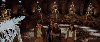 Movie still from “Indiana Jones and the Kingdom of the Crystal Skull” (2008), directed by Steven Spielberg – A group of people standing in a room with statues; Wide shot, Low angle