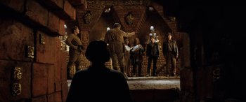 Movie still from “Indiana Jones and the Kingdom of the Crystal Skull” (2008), directed by Steven Spielberg – A group of people standing on a stage in the dark; Wide shot, Over the shoulder angle