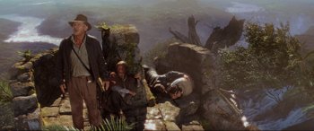 Movie still from “Indiana Jones and the Kingdom of the Crystal Skull” (2008), directed by Steven Spielberg – A man laying on the ground next to a cliff; Wide shot, High angle