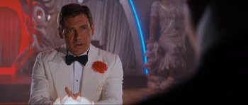 Movie still from “Indiana Jones and the Temple of Doom” (1984), directed by Steven Spielberg – A man in a white suit with a red flower in his lapel; Medium shot, Over the shoulder angle