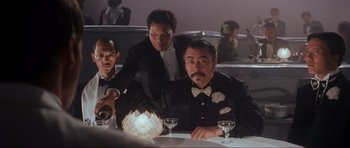 Movie still from “Indiana Jones and the Temple of Doom” (1984), directed by Steven Spielberg – A group of men sitting at a table with a lit candle; Medium shot, Low angle