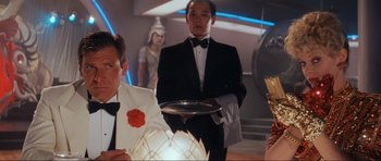 Movie still from “Indiana Jones and the Temple of Doom” (1984), directed by Steven Spielberg – A man holding a tray in front of other people in a room; Medium shot, Low angle