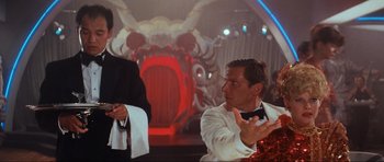Movie still from “Indiana Jones and the Temple of Doom” (1984), directed by Steven Spielberg – A man in a suit and tie talking to another man in a suit and tie; Medium shot, Over the shoulder angle